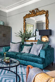 Blue velvet sofa with cushions and an antique mirror above in a living room