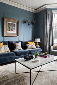 Klassisches Wohnzimmer mit blauen Wänden, farblich passendem Samtsofa und gelben Akzenten
