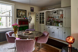 Runder Esstisch mit Marmorplatte, Stühle mit rosa Samtbezug und Anrichte im Esszimmer