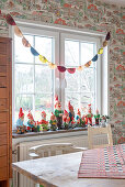 Garden gnome collection on a windowsill in the dining room with vintage wallpaper