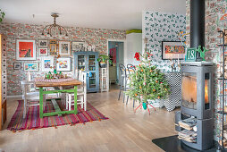 Spacious dining room with vintage furnishings, pictures on wallpapered walls, Christmas tree and wood-burning stove in the foreground