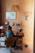 Mädchen am Schreibtisch im Kinderzimmer mit heller Holzverkleidung