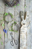 Easter bunny cut out of birch bark with a wreath of birch twigs and grape hyacinths (Muscari), Easter decoration on the terrace