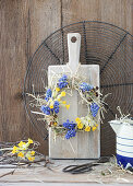 Wreath of grape hyacinths (Muscari), primroses (Primula veris), primroses and hay on a wooden board in front of a cooling rack