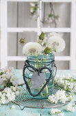 Dandelions in a glass with hearts made of string and sheet metal, in front of a window