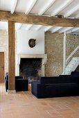 Dark blue sofa in front of fireplace in living room with natural stone wall and terracotta tiled floor