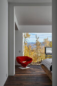 Blick ins Gästezimmer mit raumhoher Glaswand und rotem Stuhl