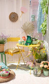 Farbenfroher Balkon mit gelbem Klapptisch, Stuhl, grünem Hocker und Pflanzenarrangement