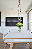 Moderne Küche mit weißem Tisch, Hängeleuchten und Blumenstrauß in minimalistischem Design