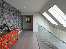 Upper floor hallway with glass railing and large skylights, red chest and sculpture