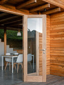 Blick von der Terrasse durch offene Tür auf Essbereich mit weißem Tisch und Stühlen, Holzverkleidung