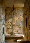 Shower with rough stone tiles and concrete bench in Mexican bathroom