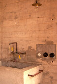 Concrete washbasin with tap and rustic pendant light, interior design in raw concrete look