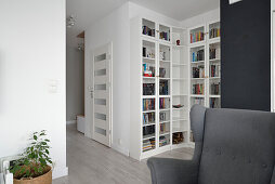 Wohnzimmer mit großem Bücherregal und grauem Ohrensessel