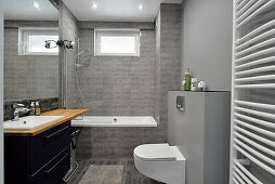 Modernes Badezimmer mit grauen Fliesen und dunklem Waschbecken-Unterschrank