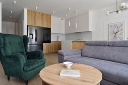 Modern living room with grey sofa, green armchair and open kitchen in wood and white tones