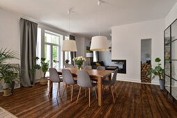 Dining area with wooden table and grey chairs, plants and fireplace in the open-plan living room