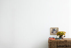 Woven chest with books and flower arrangement in front of white wall