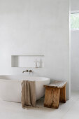 Freestanding bathtub with wooden bench in minimalist bathroom