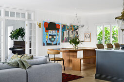 Modern living and dining area with wooden table, artwork, grey sofa and piano