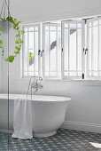 Freestanding bathtub in front of mullioned windows in the bright bathroom