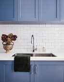 Blue kitchen cabinets and white tiled wall with stainless steel sink