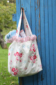 Self-sewn bag made of rose fabric with ruffles on a blue wooden door in the garden
