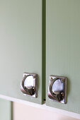 Metal handles on pastel green kitchen cabinet doors