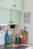 Corner of a retro-style kitchen with green cupboards and thermos flasks