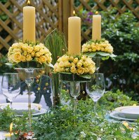 Yellow candles with roses in glass candlesticks on table