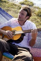 Young man sitting in a hammock playing a guitar