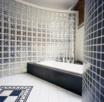 Loft-Badezimmer mit Wanne in steinverkleidetem Podest vor gebogener Glasbaustein-Wand und traditionellem Fliesenmuster am Boden