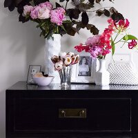 Vases of flowers, photos and handbag on black chest of drawers