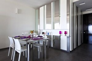 A dining table laid for a meal with a built-in steel and glass cupboard acting as a wall between rooms