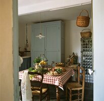 Blick in ländliche Küche mit Gemüse und Kräutern auf Esstisch, Holzschrank & Weinregal im Hintergrund
