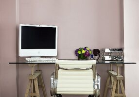 A work table with a computer resting on top of wooden saw horses and a white leather office chair in front of a pastel colored wall