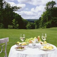 Tisch mit Oliven, Obst, Käse und Weißwein im Freien