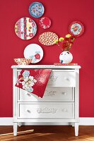 Decorative plates on red wall above white chest of drawers