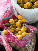 Fresh nisperos (Eriobotrya japonica) in pink plastic bags on a market stall