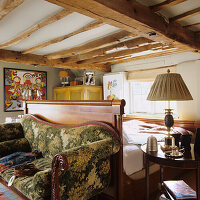 Wooden bed and vintage sofa with floral pattern in rustic bedroom with wooden beamed ceiling