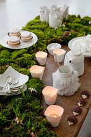Dessert table decorated with early bloomers and moss with macaroons, candles and white crockery