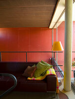 Wohnzimmer mit roter Wand, brauner Couch und gelber Stehleuchte
