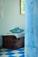 Antique wooden chest with blanket and cushions on blue and white chequered floor