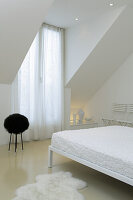 Minimalist bedroom in white with sloping ceiling and fur rug