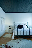 Schlafzimmer mit schwarzem Metallbett und dunkler Holzdecke