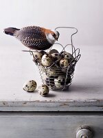 A decorative bird perched on a wire basket of quail's eggs