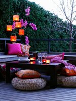 Gedeckter Tisch auf Terrasse bei Abenddämmerung mit Lampions, Blumenschmuck & Bodenkissen