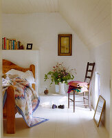 Holzbett mit gemusterter Decke, Blumenstrauß und Holzboden im Dachgeschosszimmer