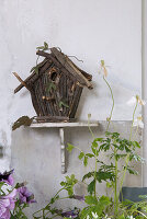 Birdhouse made of natural materials on a shelf, surrounded by anemones and petunias in the garden