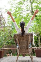 Woman sitting on garden chair with arms stretched out on terrace
